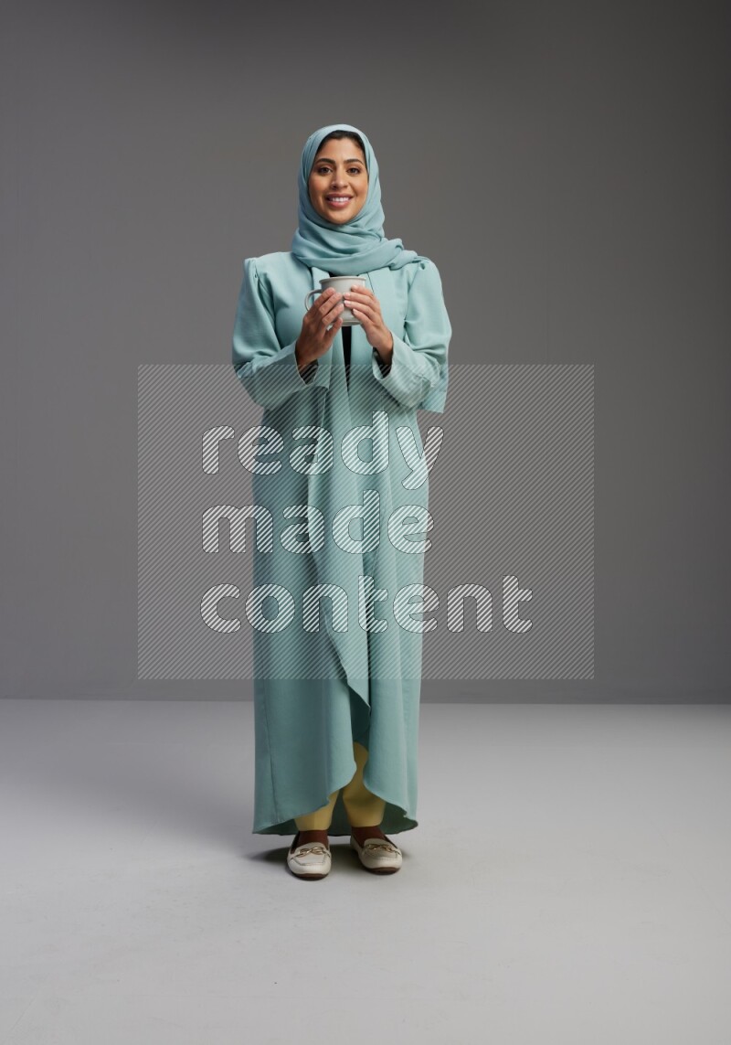 Saudi Woman wearing Abaya standing  holding a mug on Gray background