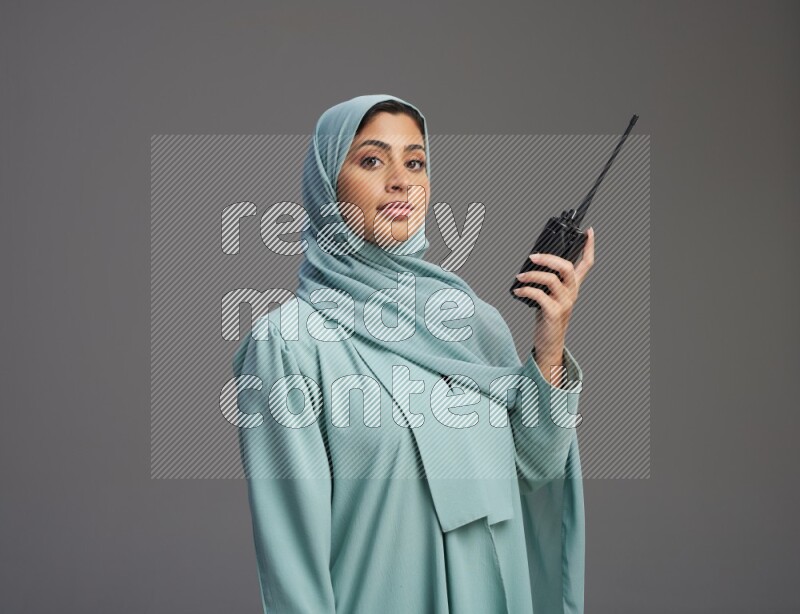 Saudi Woman wearing Abaya standing holding walkie-talkie on Gray background