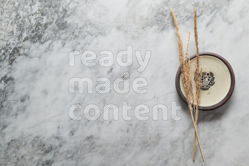 Wheat stalks on decorative pottery plate on grey marble background