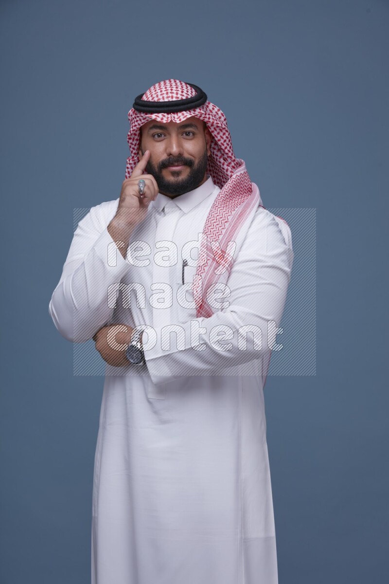 A Saudi man posing on blue background wearing Thob and Shomag