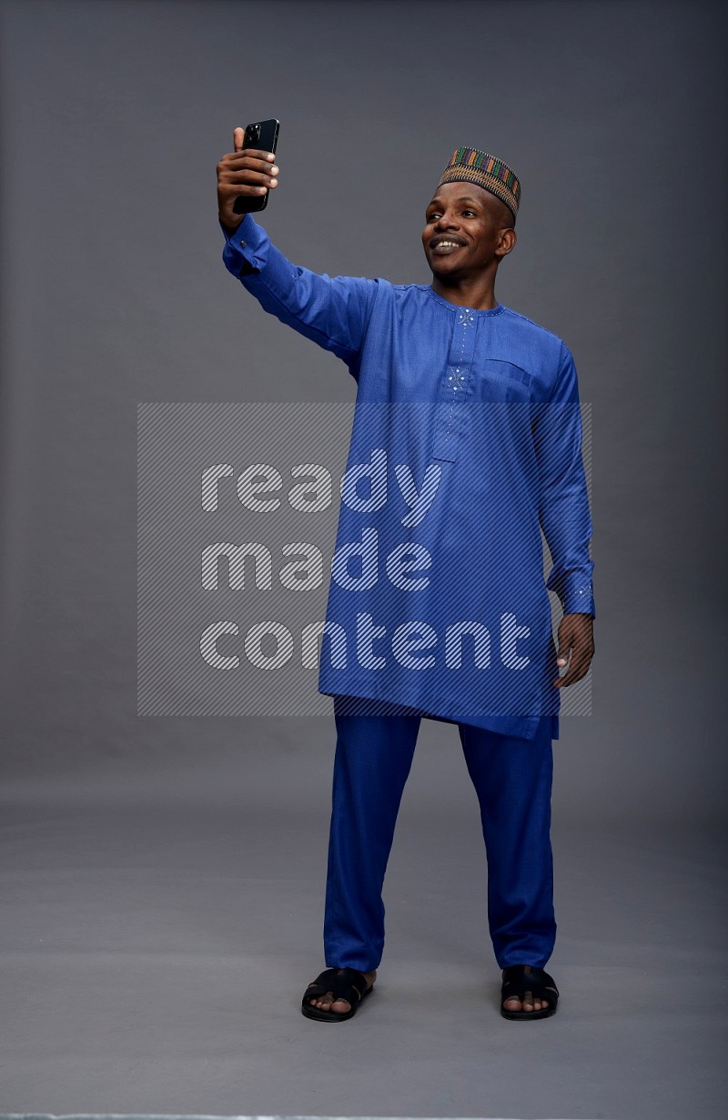 Man wearing Nigerian outfit standing taking selfie on gray background