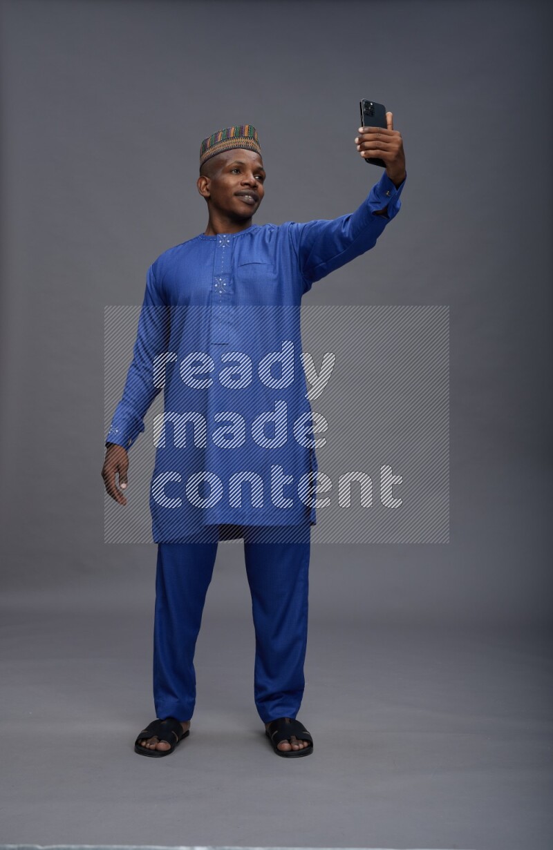 Man wearing Nigerian outfit standing taking selfie on gray background