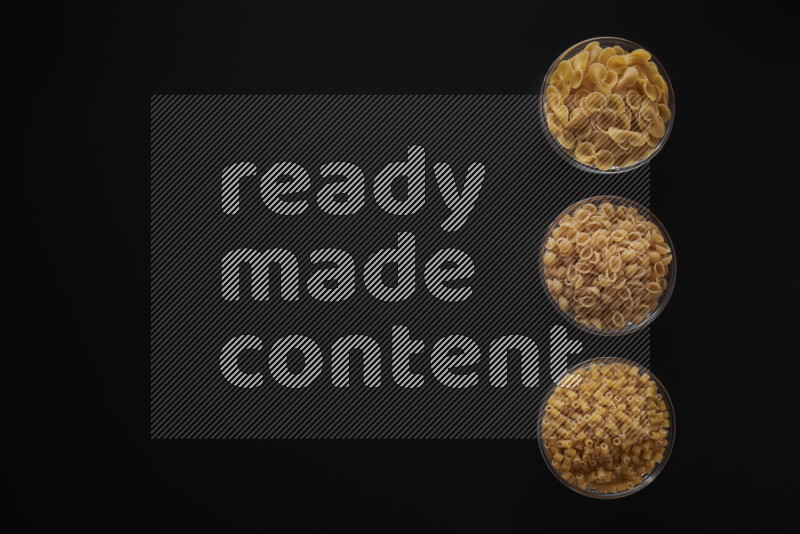 Different pasta types in 3 glass bowls on black background