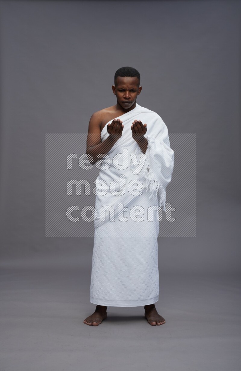 A man wearing Ehram Standing dua'a on gray background