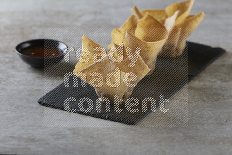 wonton cups with soy sauce ramkin on rectangle slate on grey textured counter top
