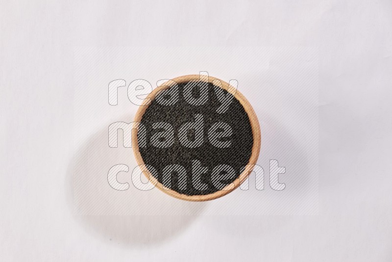 A wooden bowl full of black seeds on a white flooring