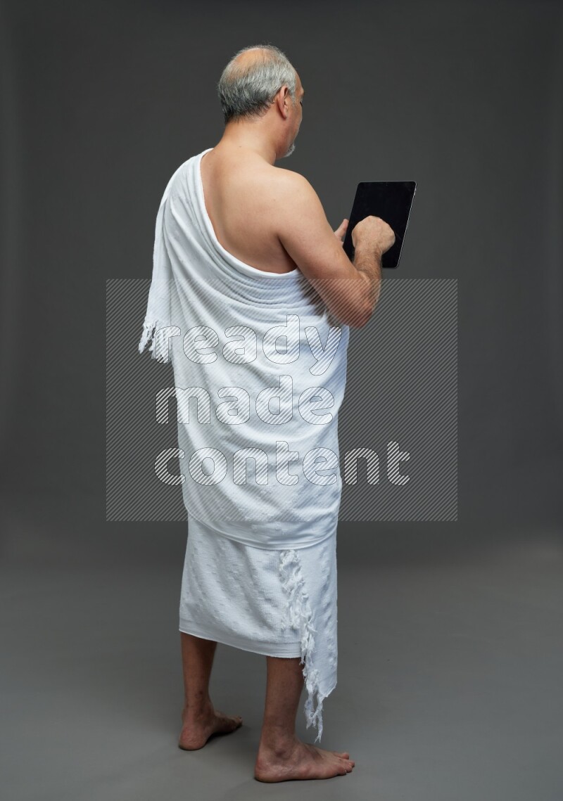 A man wearing Ehram Standing working on tablet on gray background