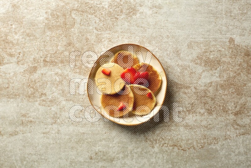 Five stacked strawberry mini pancakes in an irregular plate on beige background