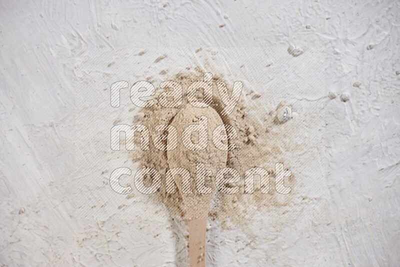 A wooden spoon full of garlic powder with scattered powder around it on a textured white flooring