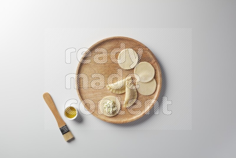 two closed sambosas and one open sambosa filled with cheese while oil with oil brush aside in a wooden dish on a white background