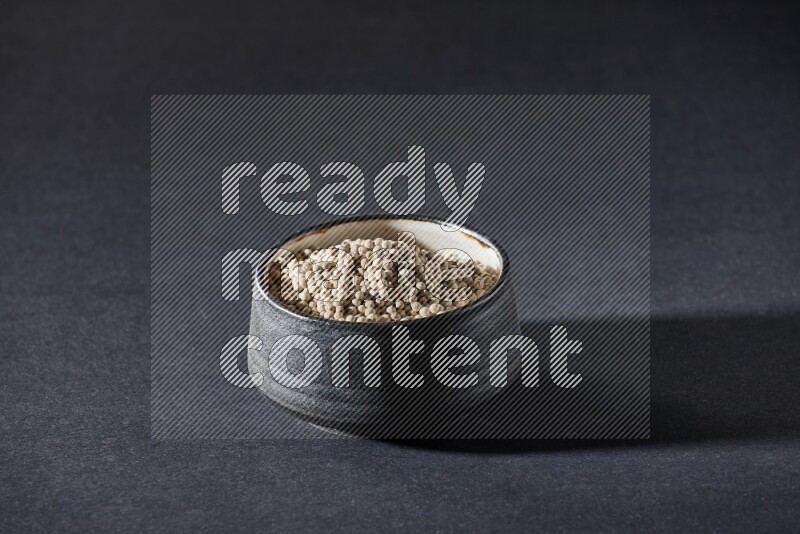 Black pottery bowl full of white pepper on black flooring