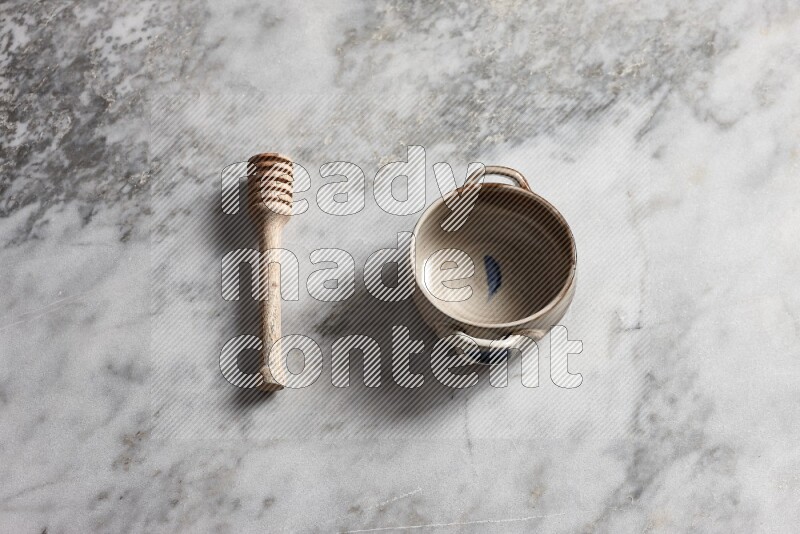 Multicolored pottery bowl with wooden honey dipper on the side on grey marble background
