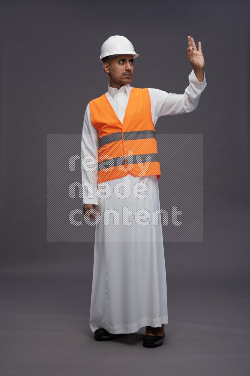 Saudi man wearing thob with engineer vest standing interacting with the camera on gray background