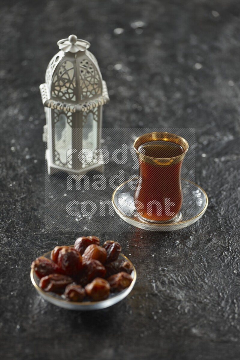 A white lantern with different drinks, dates, nuts, prayer beads and quran on textured black background