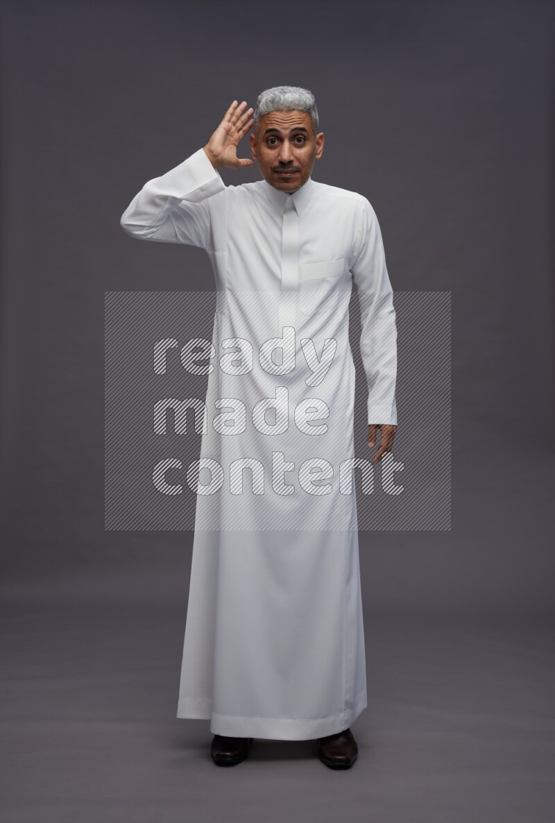 Saudi man wearing thob standing interacting with the camera on gray background
