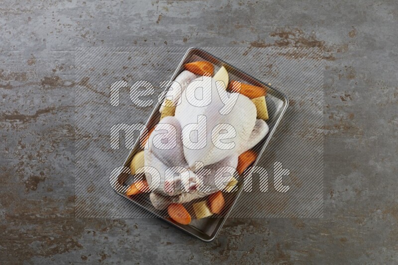 whole Raw chicken on a small oven trey direct on a rustic grey background