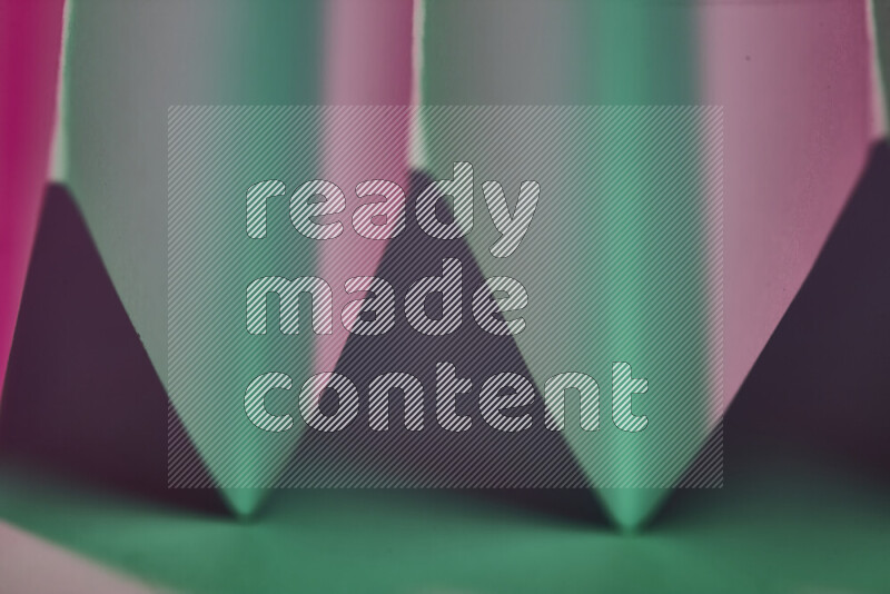 A close-up abstract image showing sharp geometric paper folds in green and pink gradients