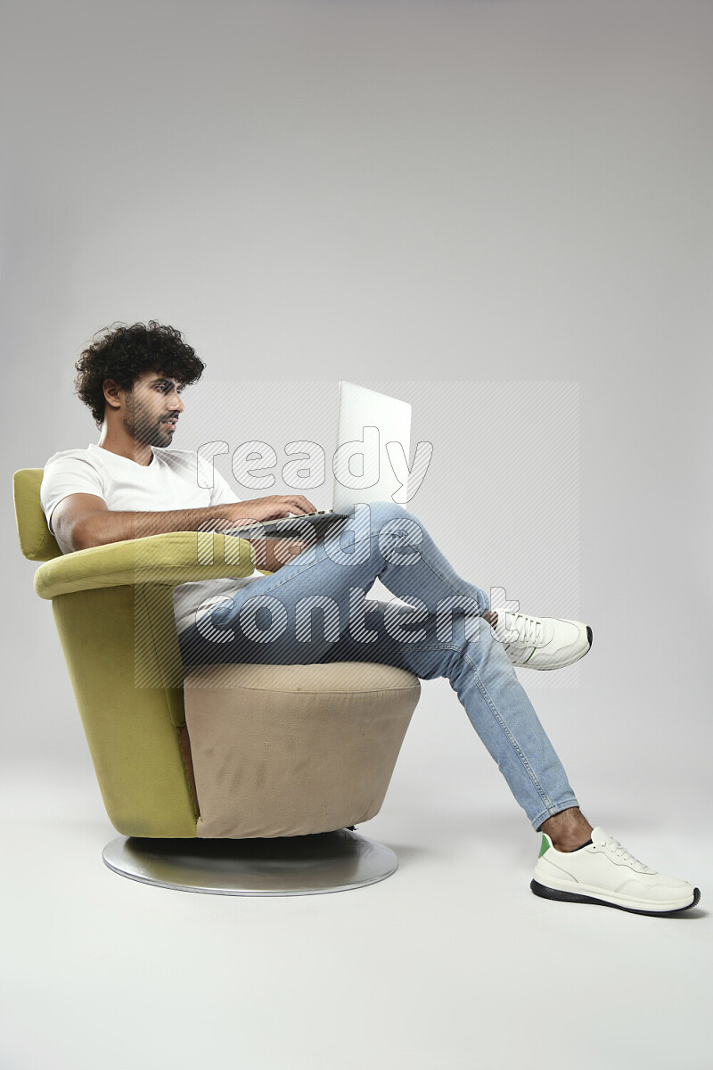 رجل يرتدي ملابس كاجوال يجلس علي كرسي و يعمل علي لاب توب علي خلفية بيضاء
