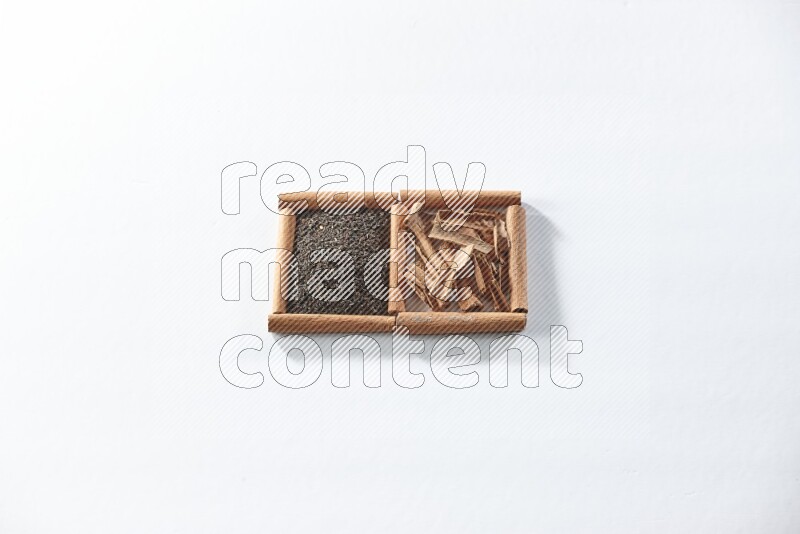 مربعان من أعواد القرفة ممتلئان بالشاي الأسود وقطع القرفة علي خلفية بيضاء