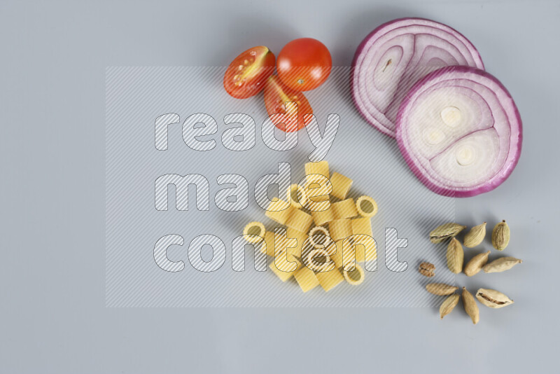Raw pasta with different ingredients such as cherry tomatoes, garlic, onions, red chilis, black pepper, white pepper, bay laurel leaves, rosemary, cardamom and mushrooms on light blue background