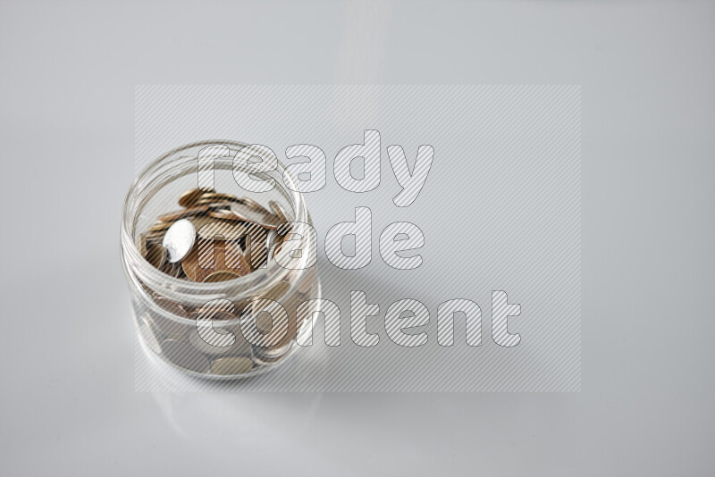 Random old coins in a glass jar on grey background