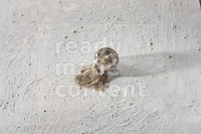 Flipped glass spice jar full of black pepper powder on a textured white flooring