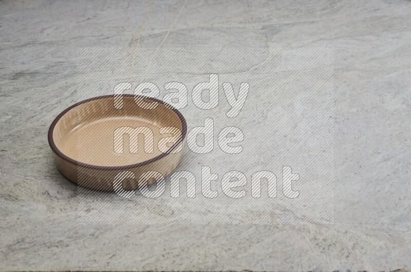 A beige pottery oven bowl on grey marble background