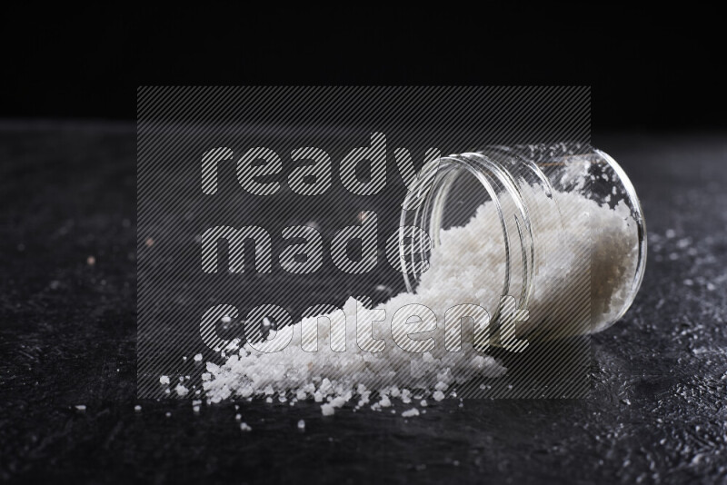 A glass jar full of coarse sea salt crystals on black background