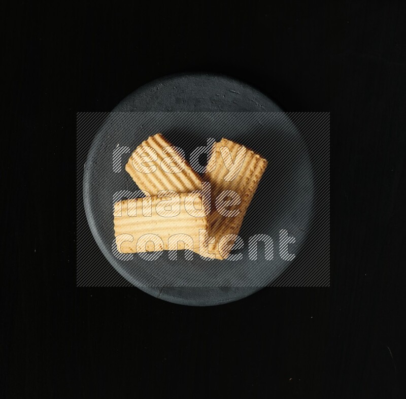 Golden biscuits in a black pottery plate on black background