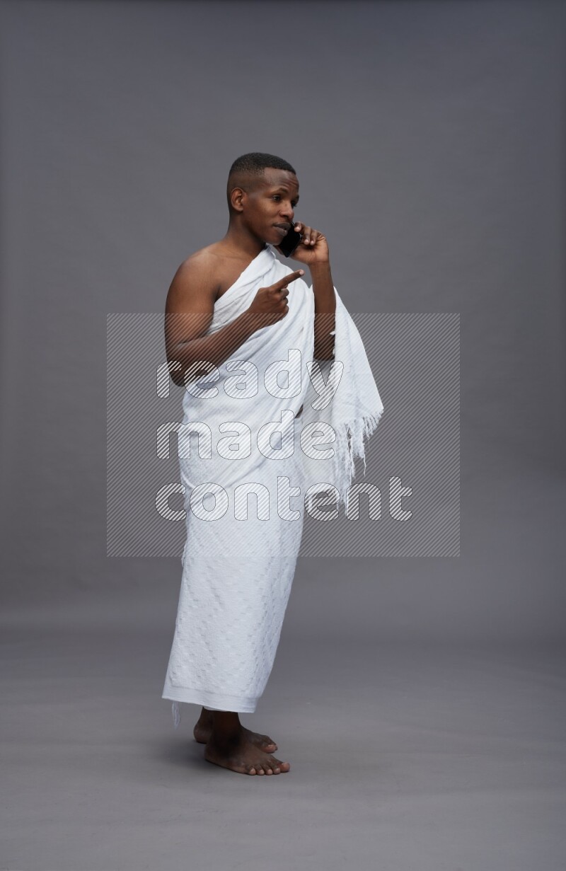A man wearing Ehram Standing talking on phone on gray background