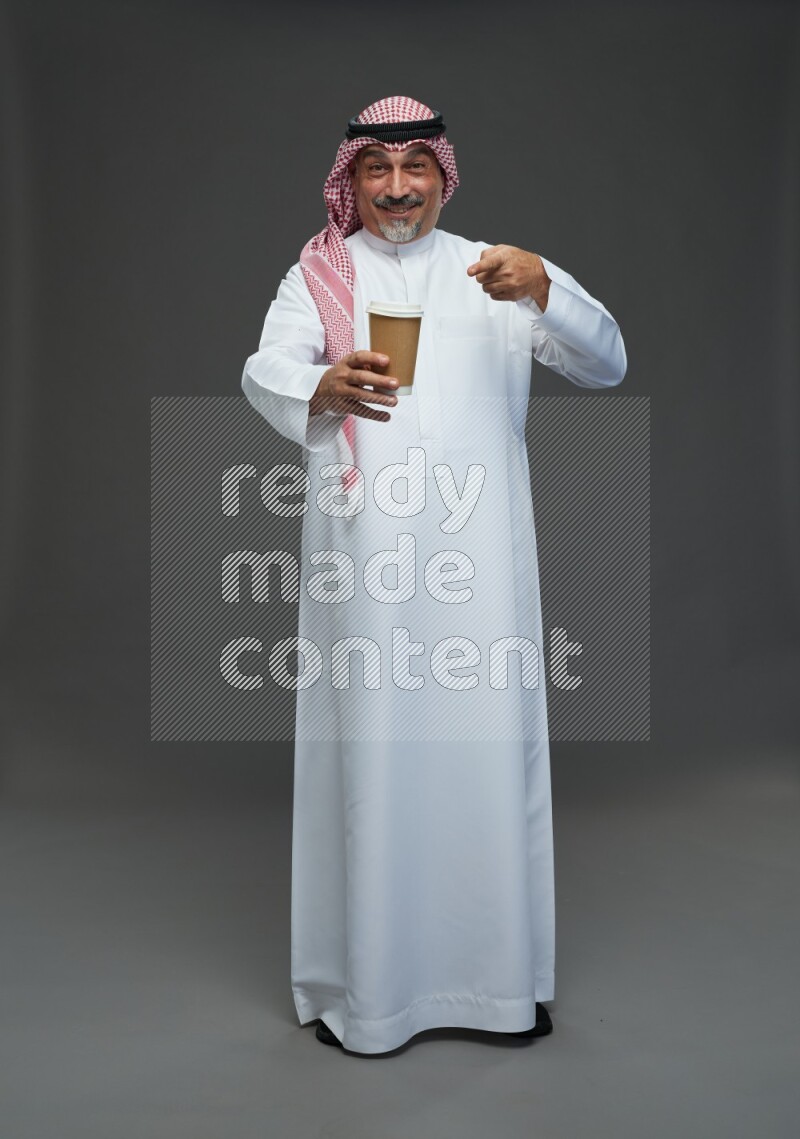 Saudi man with shomag Standing holding paper cup on gray background
