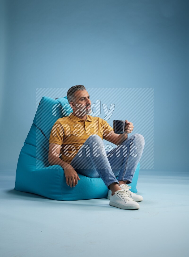 A man sitting on a blue beanbag and drinking coffee