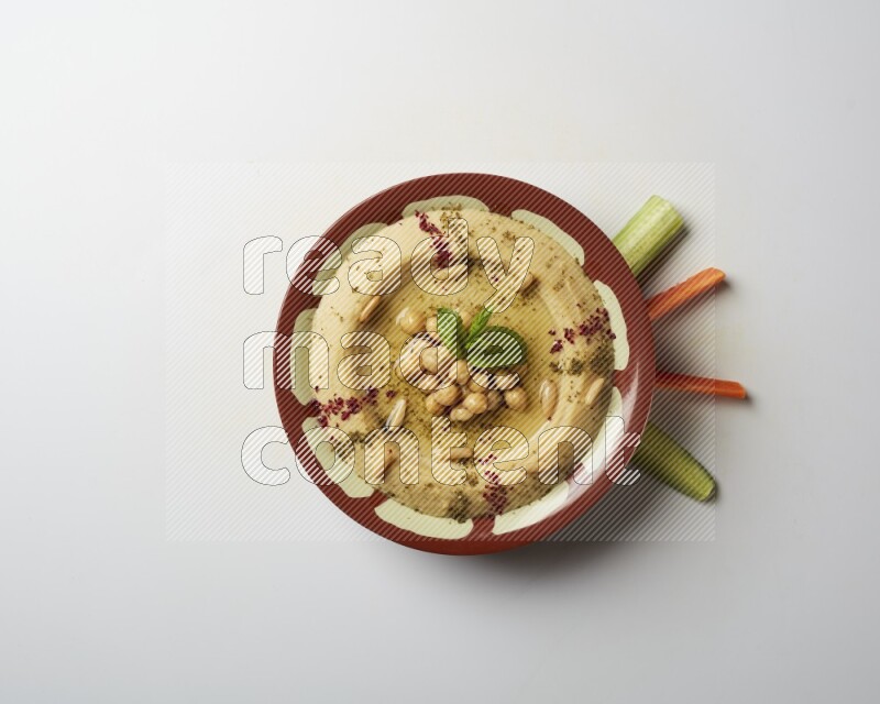 Hummus in a traditional plate garnished with zaatar & sumak on a white background