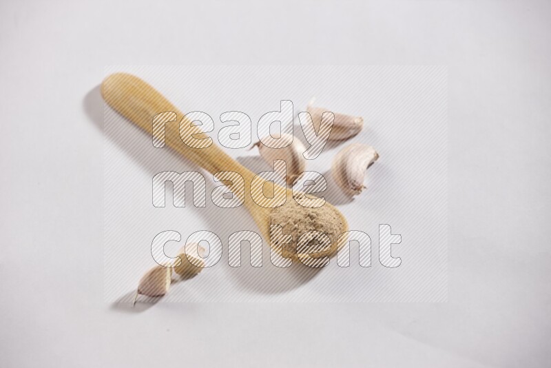 A wooden spoon full of garlic powder with cloves beside it on a white flooring