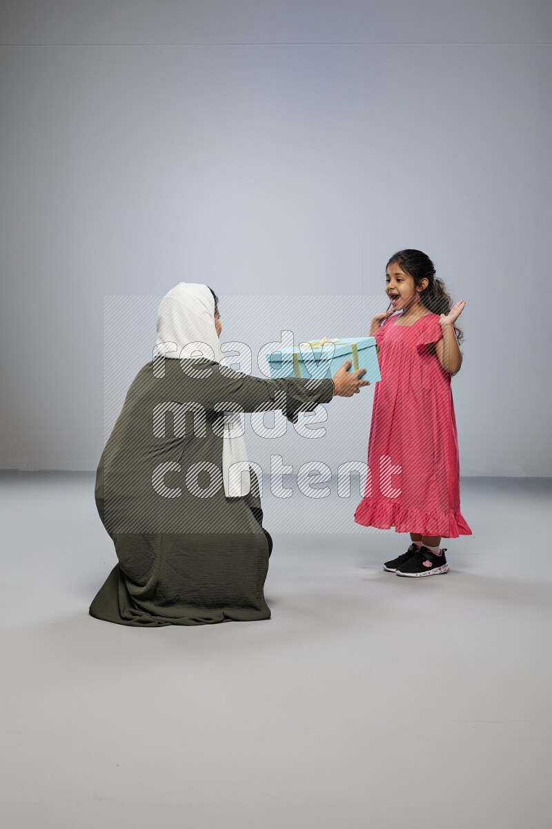 A girl giving a gift to her mother on gray background