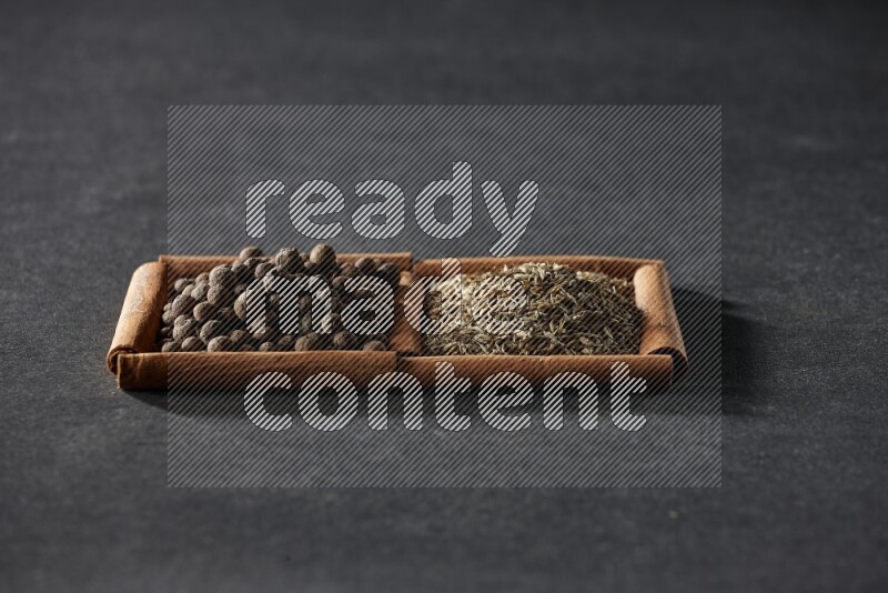 مربعان من أعواد القرفة ممتلئان بحبوب الكمون وحبوب بهار الفلفل الحلو علي خلفية سوداء