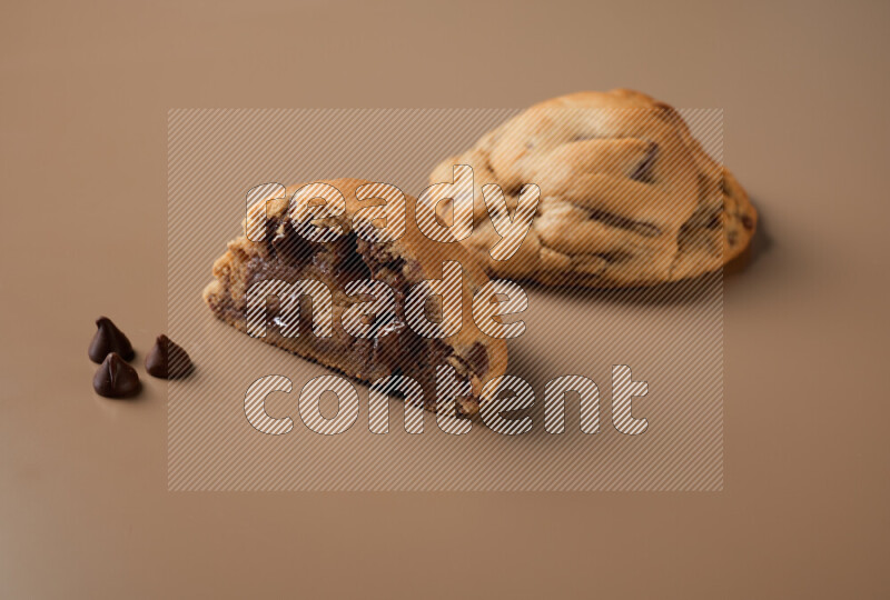 a chocolate chip cookie with another one cut in half on a brown background