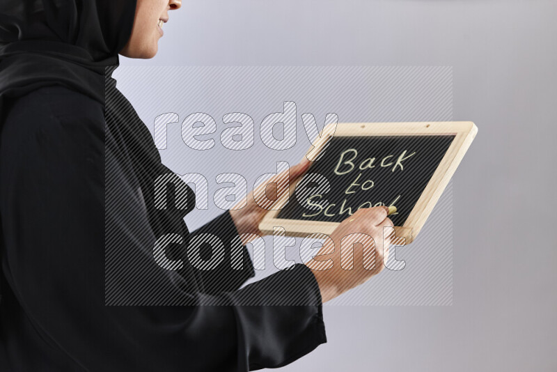A woman in abaya holding books and a board in different positions (back to school)