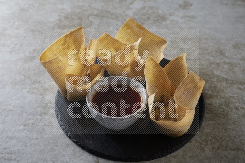 wonton cups with soy sauce ramkin on circle slate on grey textured counter top