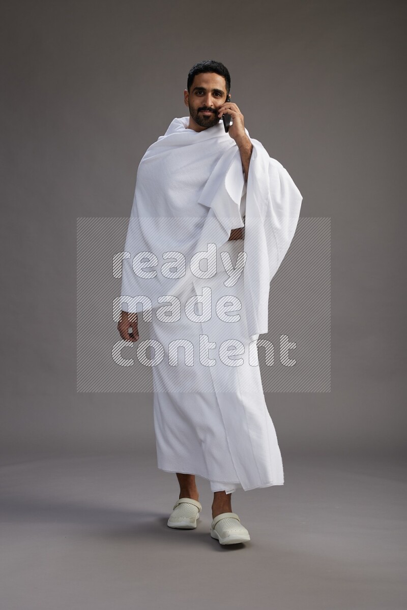 A man wearing Ehram Standing talking on phone on gray background
