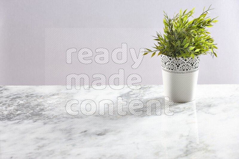Green artificial plant in white decorative pot on grey marble background