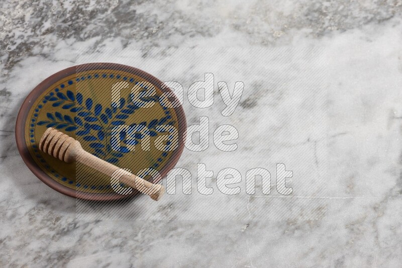 Decorative pottery plate with wooden honey dipper in it on grey marble background