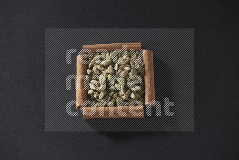 A single square of cinnamon sticks full of Cardamom on black flooring