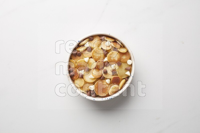 Top-view shot of mixed chocolate chips cereal pancakes in a round bowl on white background