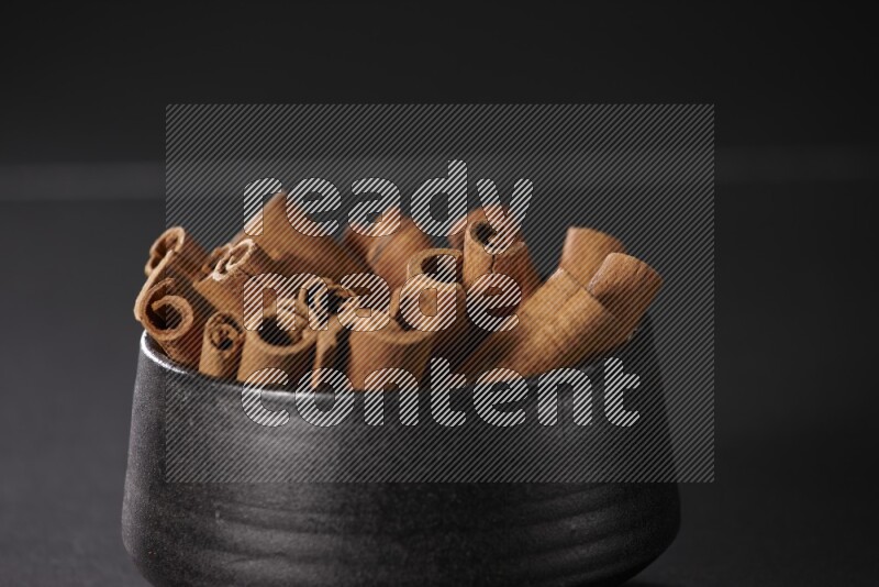 Cinnamon sticks in a black bowl on a black background in different angles