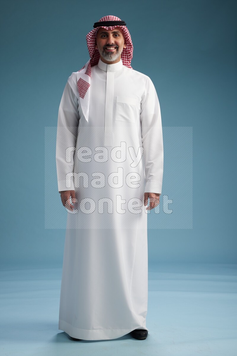 Saudi man wearing thob and shomagh posing to the camera on blue background