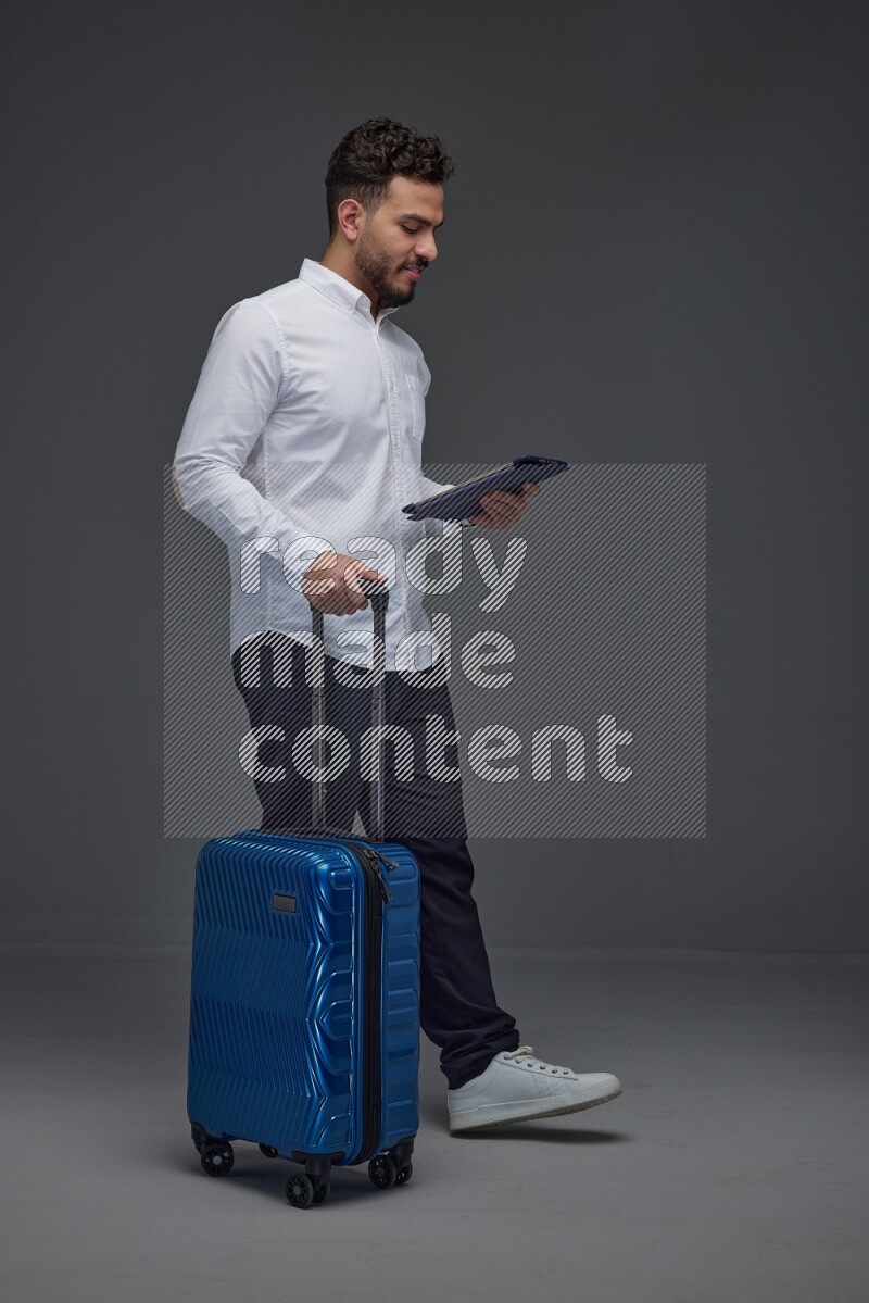 A man wearing smart casual with and pulling a carry-on luggage eye level on a gray background