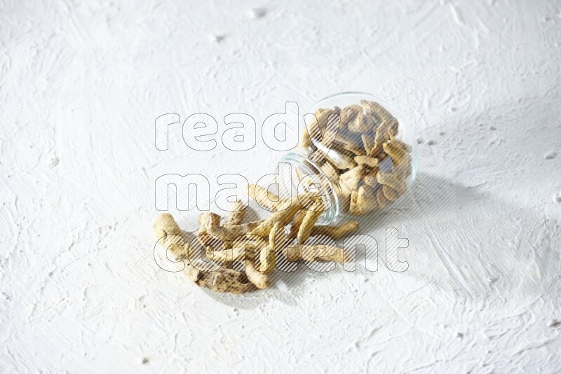 وعاء زجاجي للتوابل مقلوب وممتلئ بأصابع الكركم المجففة وتساقطت خارجه على خلفية بيضاء