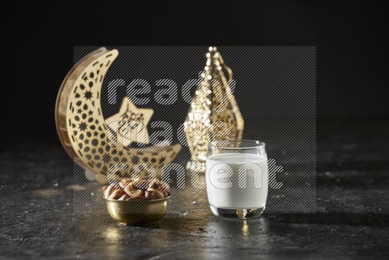 Nuts in a metal bowl with milk beside golden lanterns in a dark setup