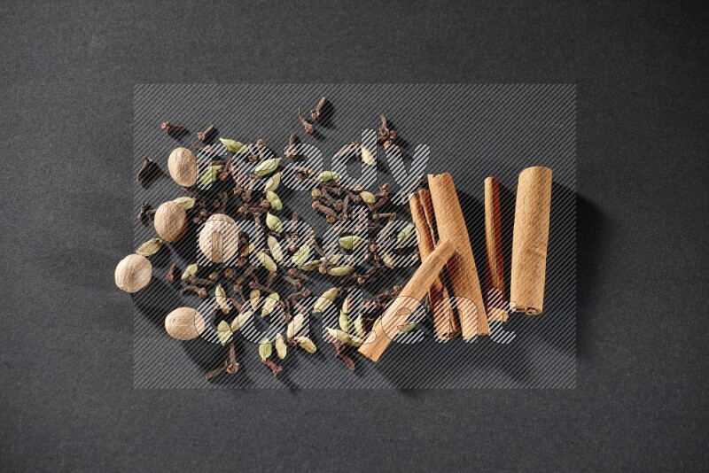 Cardamom, cloves, nutmeg and cinnamon sticks on black flooring